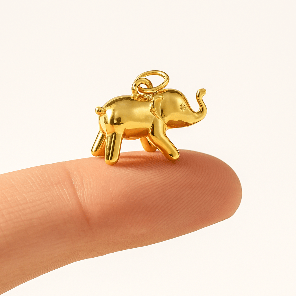 Gold elephant charm held between fingers on a white background