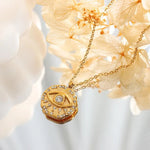 Gold necklace with a round pendant featuring a diamond, against a soft floral background.