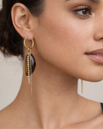 Close-up of a woman wearing a gold earring with a dark stone on a neutral background
