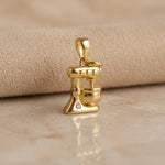 Gold pendant shaped like a mixer on a beige surface