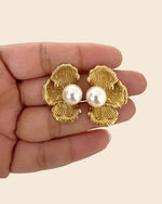 Gold earrings with pearl centers held between fingers on a beige background
