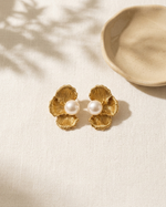 Gold floral earrings with pearl centers on a beige surface