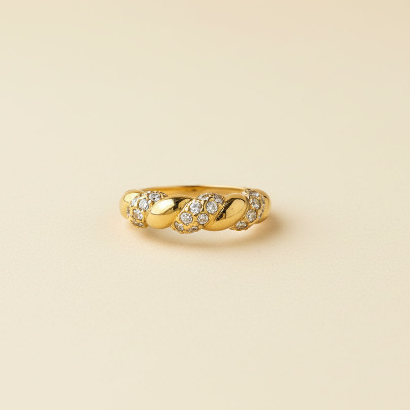 Gold ring with small diamonds on a beige cushion against a light gray background