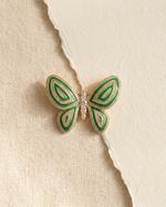 Green butterfly-shaped brooch with gold accents on a beige textured background