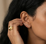 Close-up of a person wearing a gold ring and gold earring, with a neutral background.