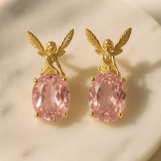 Gold angel earrings with pink gemstones on a beige background