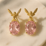 Gold angel earrings with pink gemstones on a beige background