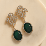 Pair of gold earrings with green gemstones on a beige background