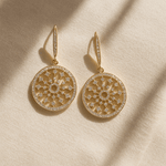 Gold earrings with intricate designs on a beige fabric background
