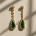 Gold earrings with green teardrop stones on a beige background