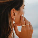 Close-up of a woman wearing gold earrings, ring, and bracelet with a blurred background