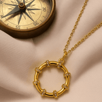 Gold necklace with circular pendant on a beige fabric background