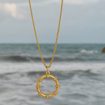 Gold necklace with a circular pendant over a blurred ocean background