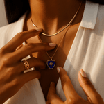 Person wearing a gold necklace with a blue pendant, holding a matching gold ring.