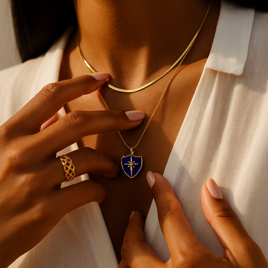 Person wearing a gold necklace with a blue pendant, holding a matching gold ring.