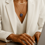 Person wearing a white blazer and gold necklace with a blue pendant, using a laptop.