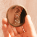 Close-up of an earring being examined in a small mirror held by a hand.