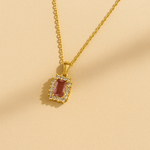 Gold necklace with a red gemstone pendant on a beige background