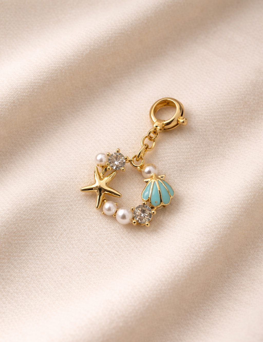 Gold charm with starfish, shell, and pearl on a beige fabric background