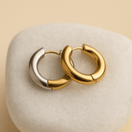 Pair of gold hoop earrings on a textured beige surface