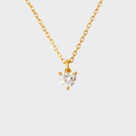A gold-colored necklace with a heart-shaped pendant that is catching light, displayed against a white background.
