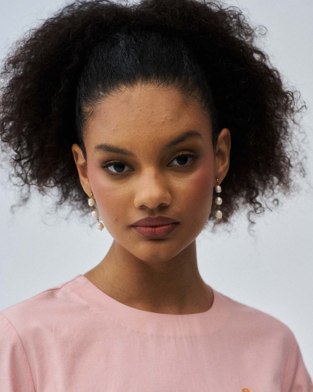 Woman with styled hair wearing a pink top against a neutral background