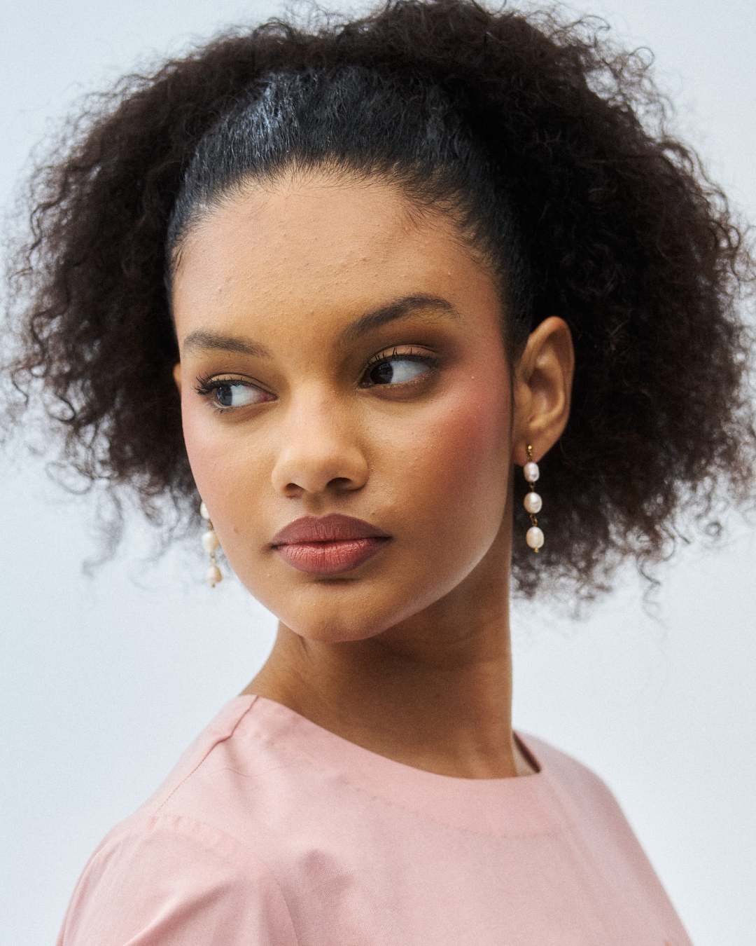 Woman with styled hair wearing a pink top against a neutral background