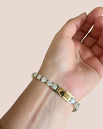 Gold bracelet with clear stones on a wrist against a beige background