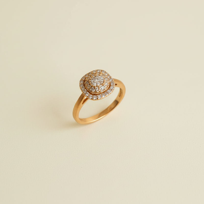 Gold ring with diamond-like stones on a beige cylindrical stand against a light gray background