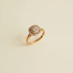 Gold ring with diamond-like stones on a beige cylindrical stand against a light gray background