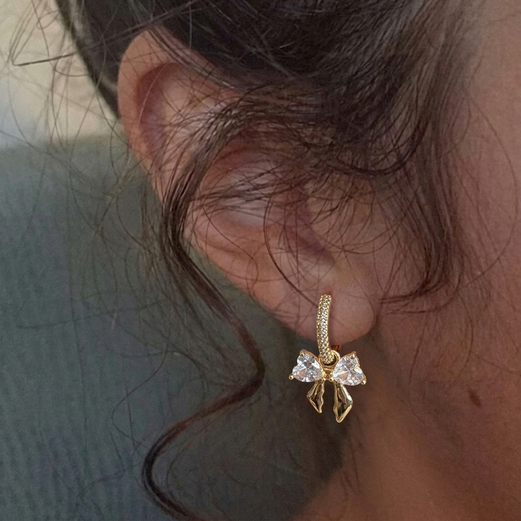 Gold bow-shaped earring worn on an ear with a neutral background