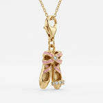 Gold pendant shaped like ballet shoes with a pink bow and diamonds on a white background