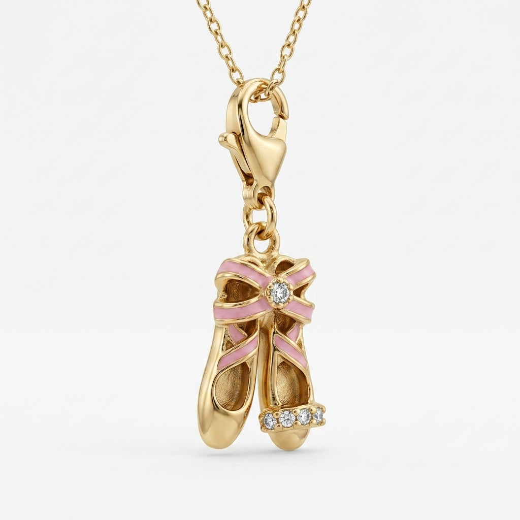Gold pendant shaped like ballet shoes with a pink bow and diamonds on a white background