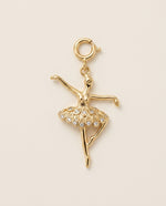 Gold ballerina charm with crystal skirt on a beige background