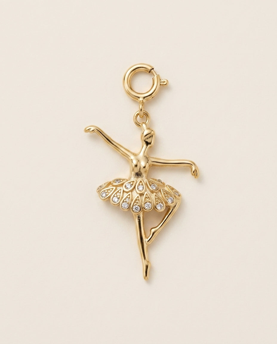 Gold ballerina charm with crystal skirt on a beige background