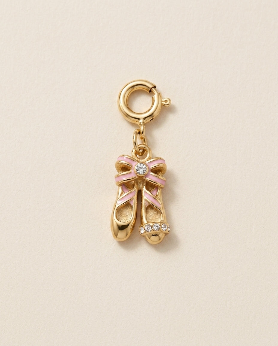 Gold charm shaped like ballet shoes with a pink bow on a beige background