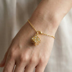 Gold bracelet with a dice-shaped charm on a wrist against a neutral background