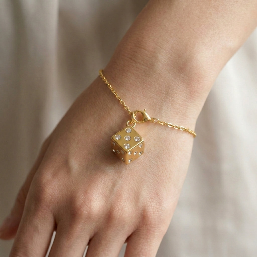 Gold bracelet with a dice-shaped charm on a wrist against a neutral background