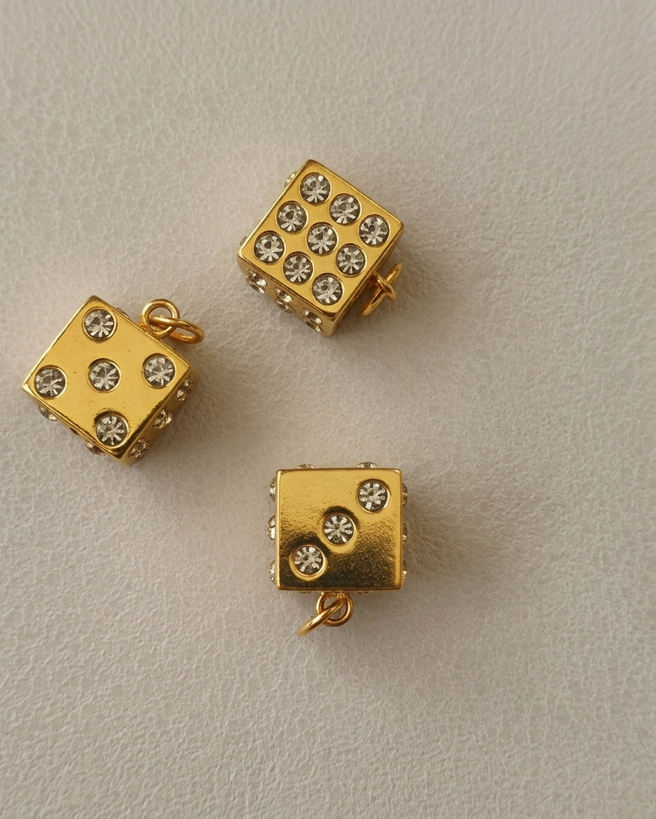 Gold dice-shaped jewelry pieces with gemstone accents on a beige background