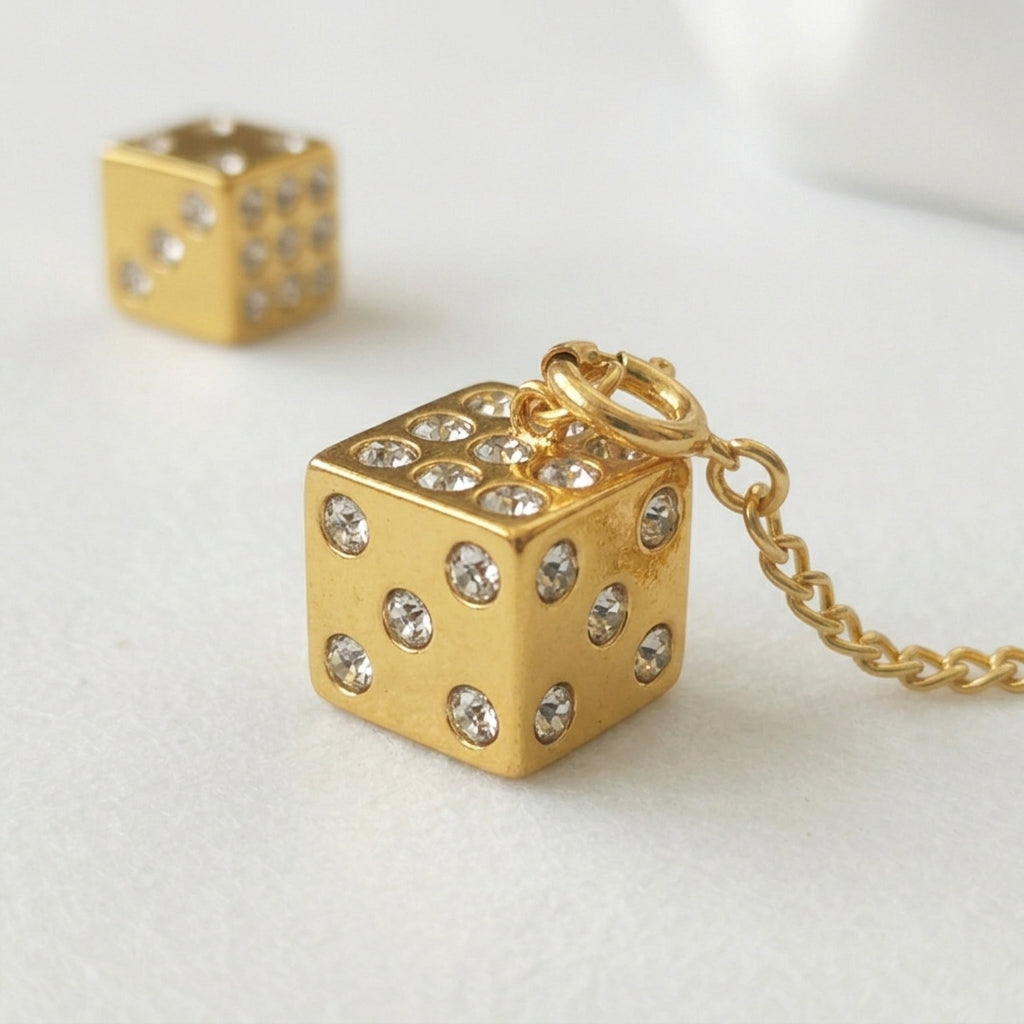 Gold dice-shaped pendant with rhinestones on a chain against a light background