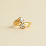 Gold ring with heart-shaped gemstones on a textured beige surface