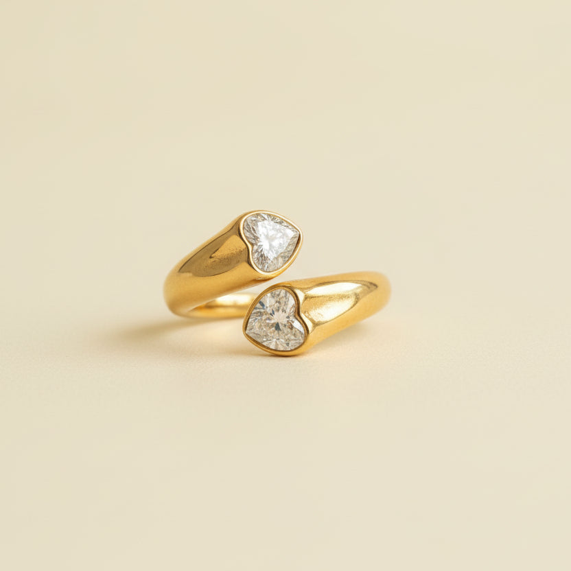 Gold ring with heart-shaped gemstones on a textured beige surface