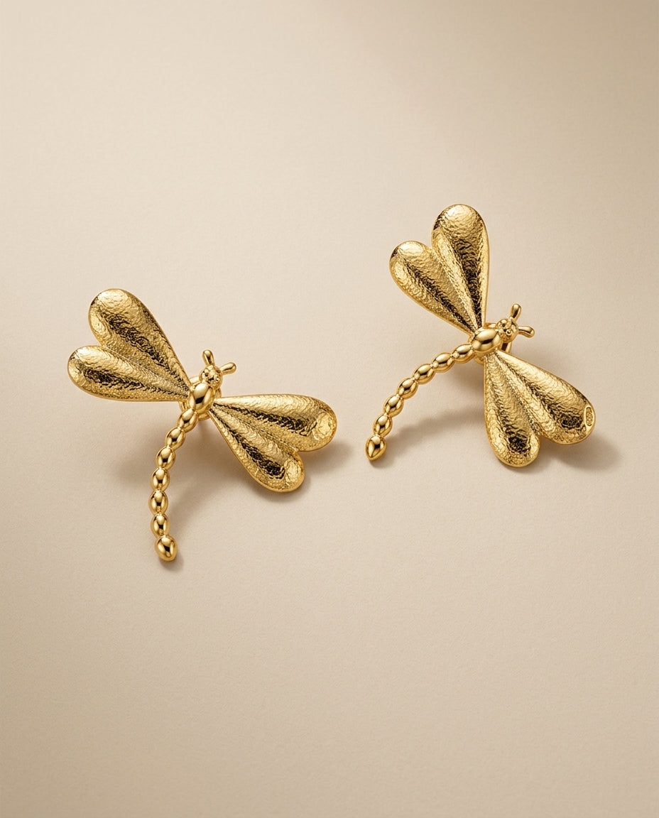Gold dragonfly earrings on a beige background