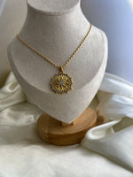 Gold necklace on a mannequin bust with a white garment in the background