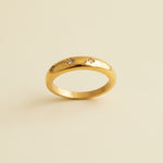 Gold ring with engraved designs on a textured beige surface