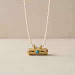 Pearl necklace with a gold and turquoise pendant on a beige background