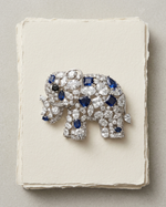 Jeweled elephant brooch with blue and clear stones on a textured white surface