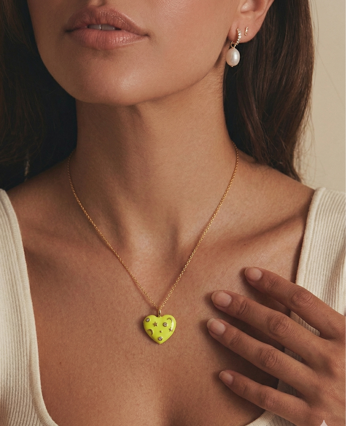 Woman wearing a yellow enamel necklace with a heart-shaped pendant, hand on chest.