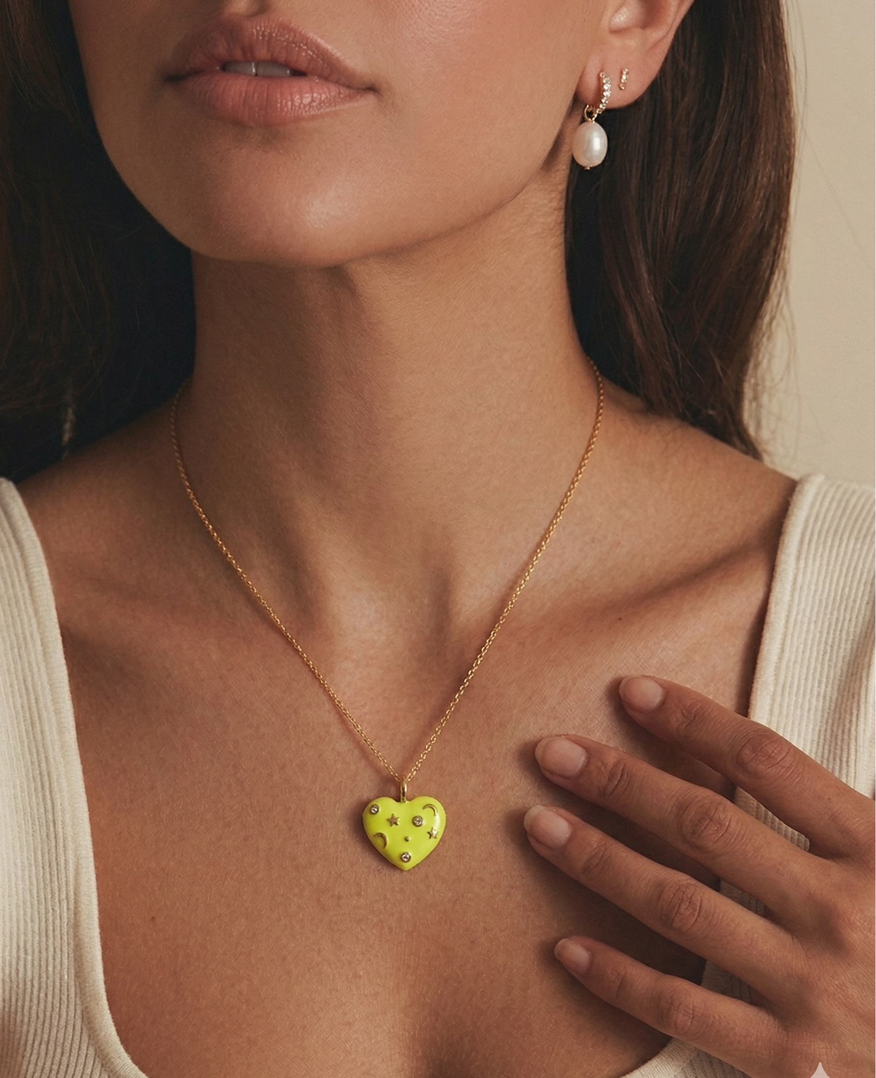 Woman wearing a yellow enamel necklace with a heart-shaped pendant, hand on chest.