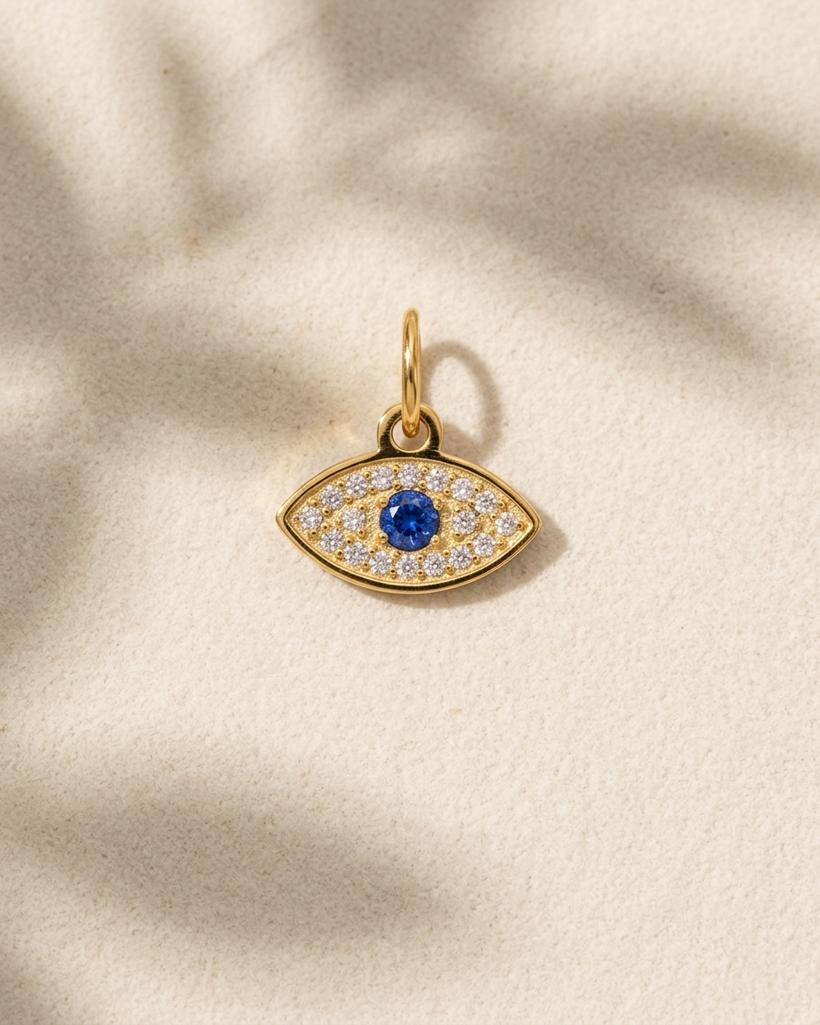 Gold evil eye pendant with a blue gemstone on a beige background